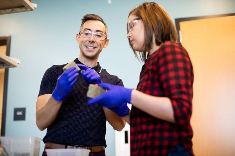 À esquerda, Wil Srubar - engenheiro estrutural da Universidade do Colorado, em Boulder. À direita, a aluna de doutorado em ciência e engenharia de materiais, Sarah Williams. Ambos segurando tijolos de matéria de construção feitos de cianobactérias