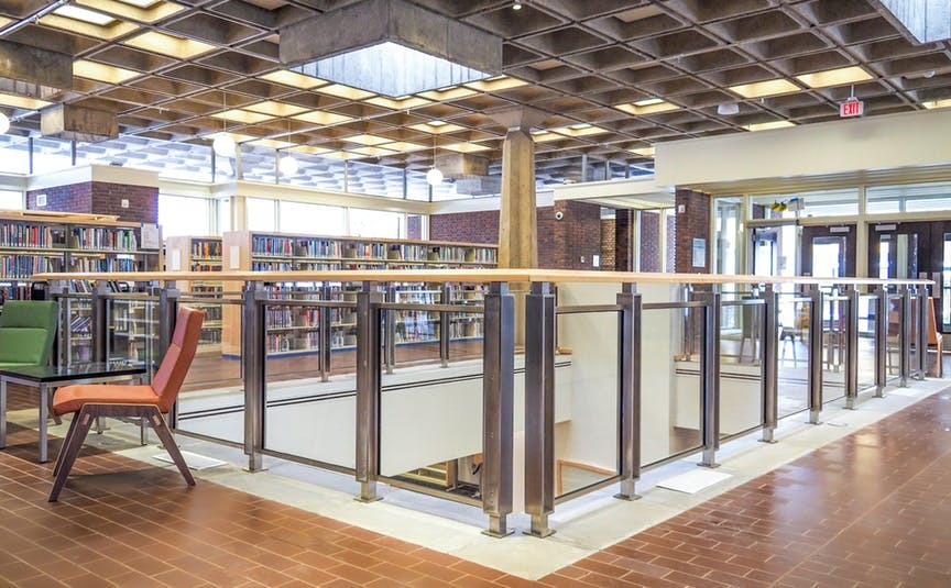 Interior do andar principal da Biblioteca Arvonne Fraser, com estantes e cadeiras. No teto, há lajes nervuradas.