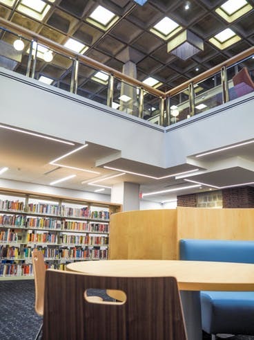Interior do andar inferior biblioteca Arvonne Fraser, com estantes, cadeiras e sofá. No teto são usadas lajes nervuradas.