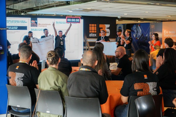 Participantes da convenção em dinâmica de equipe, diante de um telão