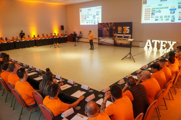 Palestra da convenção Atex Latam, com mesas em U, telões e letreiro ao fundo